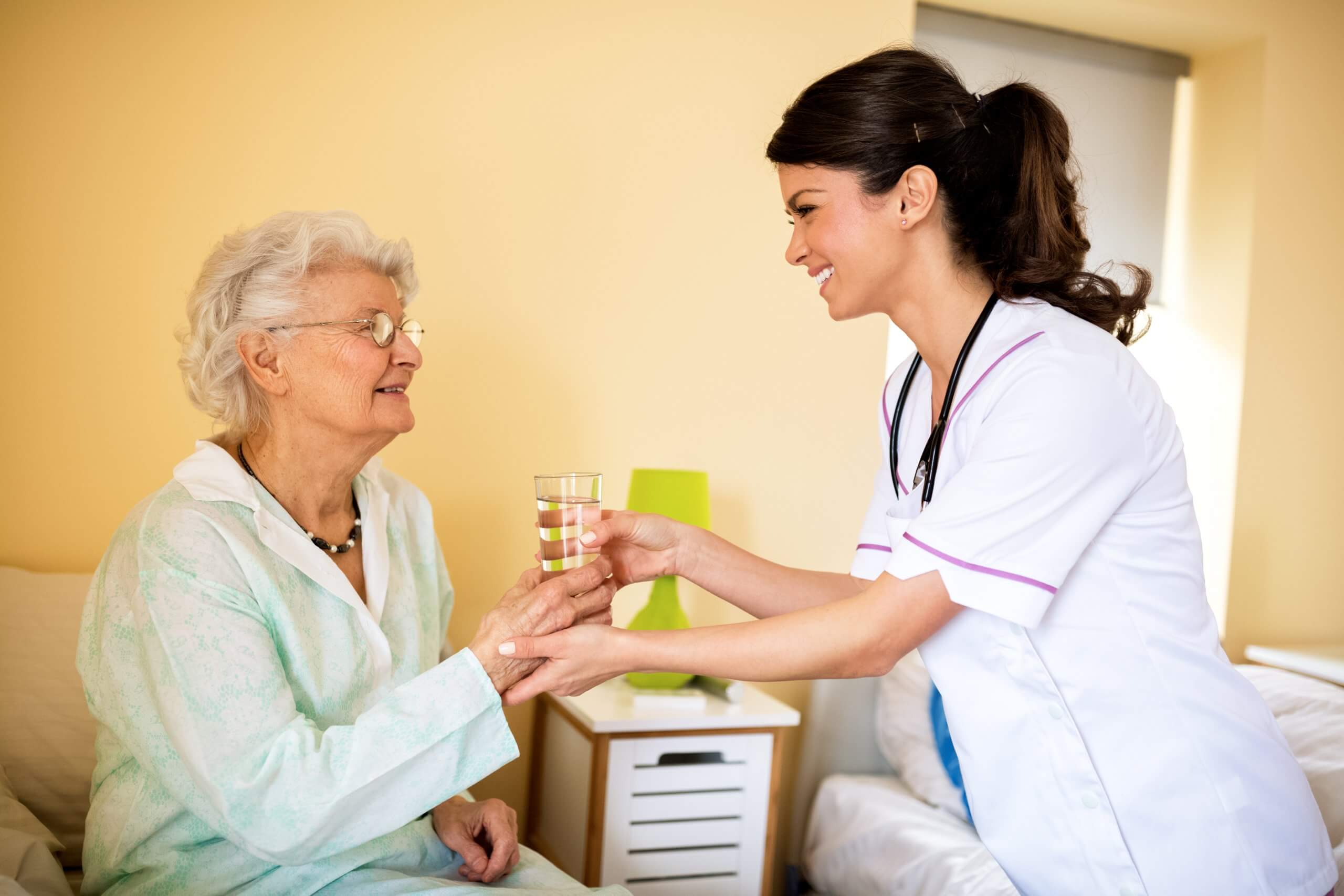 Cute,Smiling,Nurse,Brings,Water,To,Old,Patient,At,Nursing